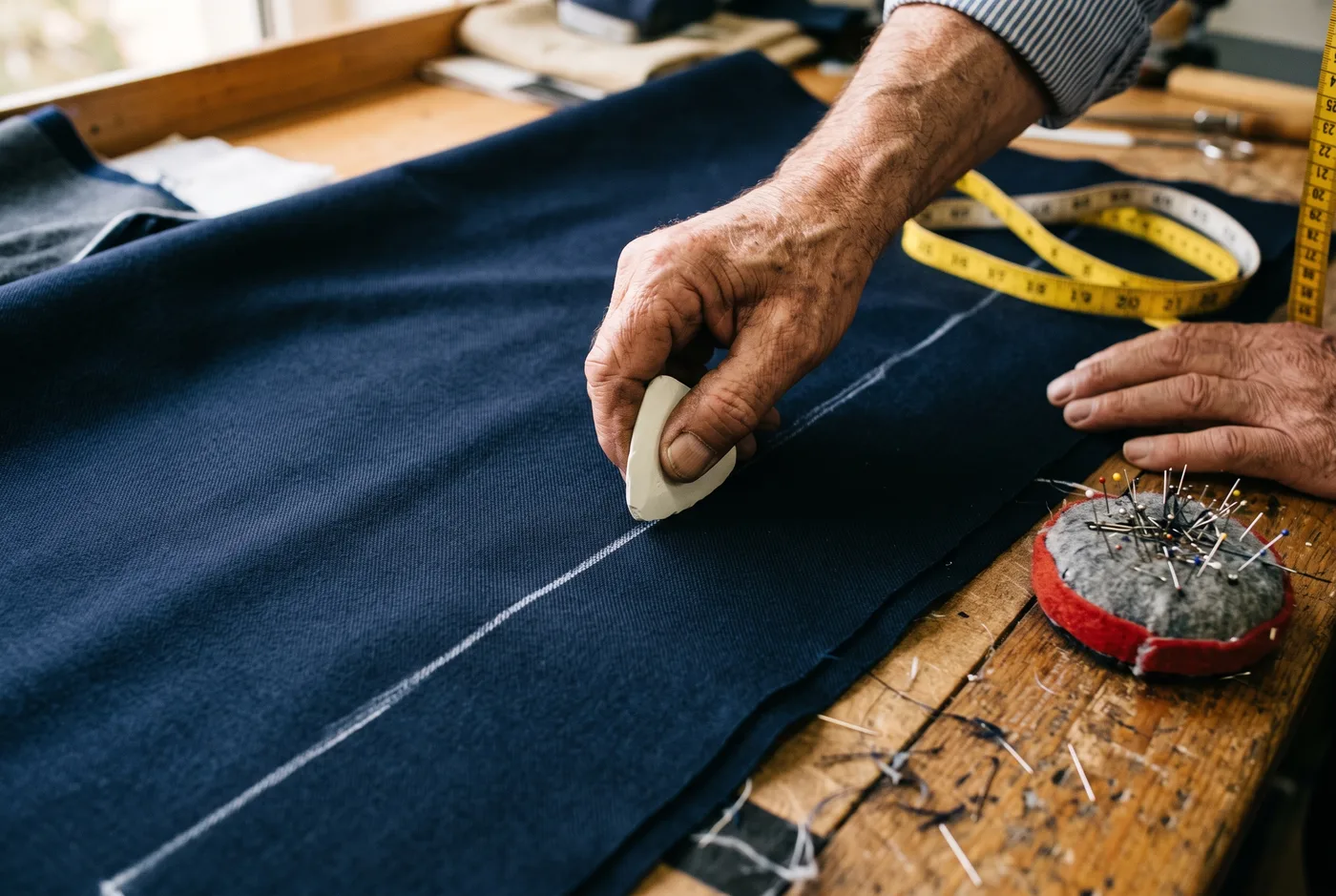 A tailor's hands marking a chalk line on navy suiting